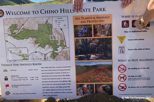 A Welcome to Chino Hills State Park is held by two hands and another set of hands measures the distance from the edge of the sign.